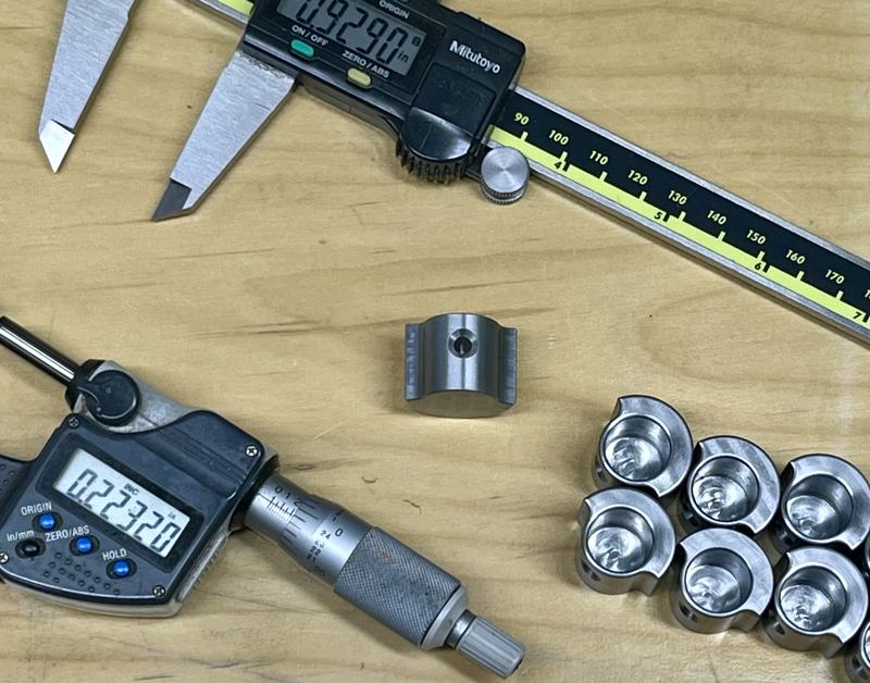 Digital calipers and a micrometer beside small machined parts on a bench