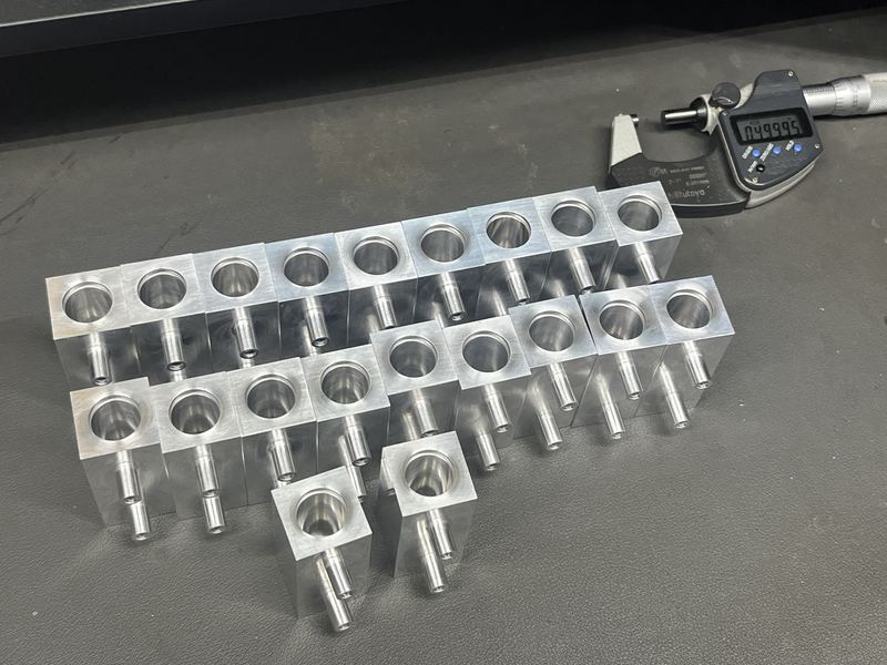 Machined aluminum manifold blocks arranged in rows beside a digital micrometer