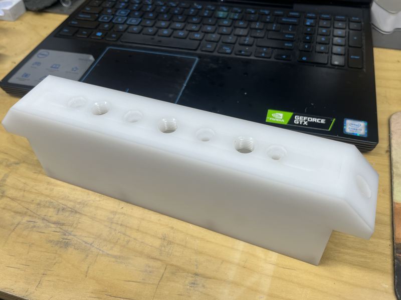 White machined plastic block with a row of tapped ports